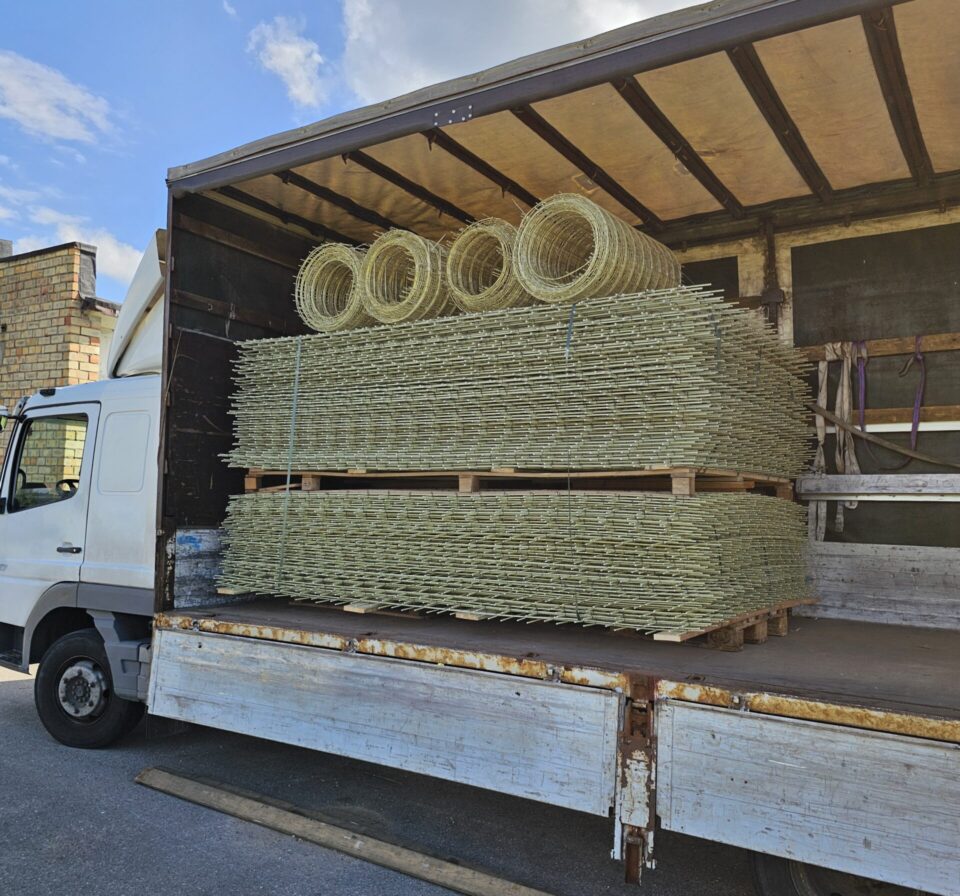 Truck loaded with GFRP reinforcement meshes and composite rebar coils stacked on pallets, secured for delivery. Fiberglass construction materials prepared for transport demonstrate efficient logistics and organized shipment of composite reinforcement products.