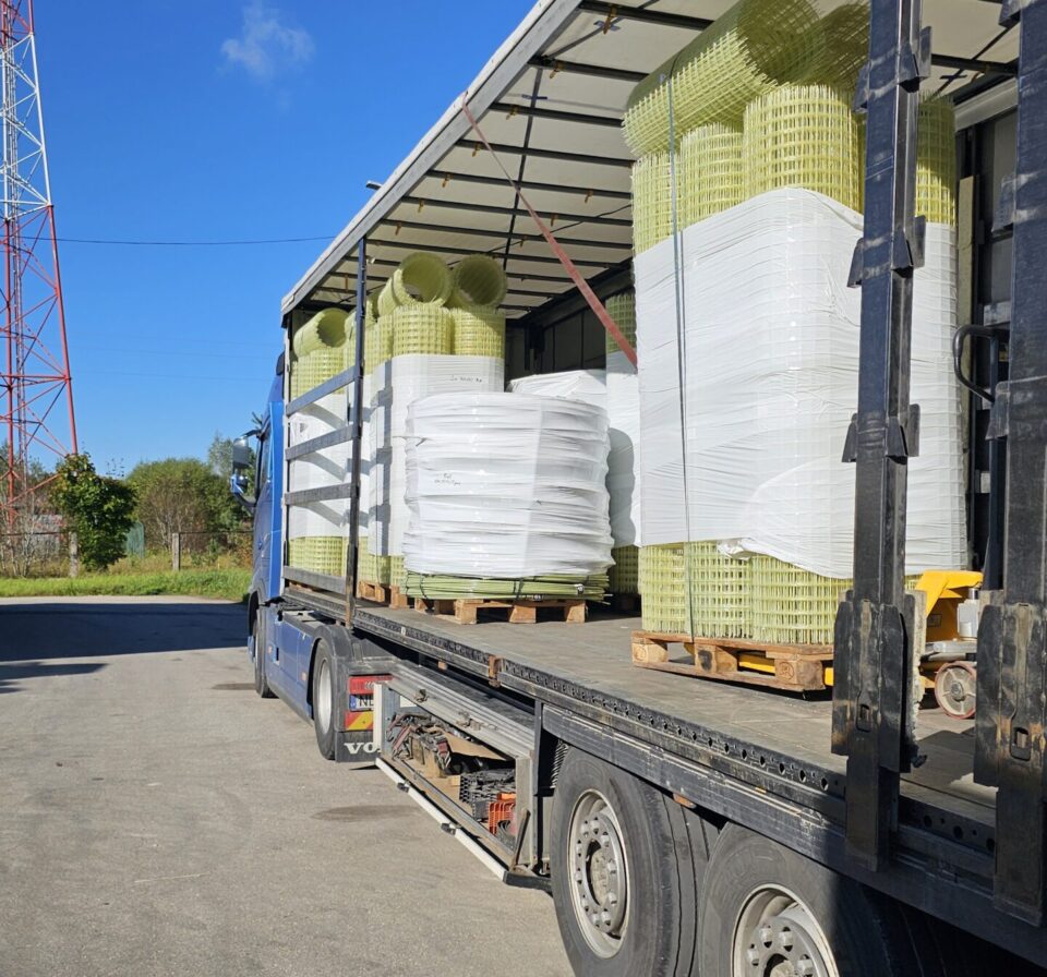Flatbed truck loaded with palletized GFRP mesh rolls and composite reinforcement materials secured for transport. Fiberglass construction products wrapped and stacked for efficient logistics and international delivery.